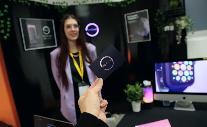 Une main tend une carte de visite Prana devant le stand