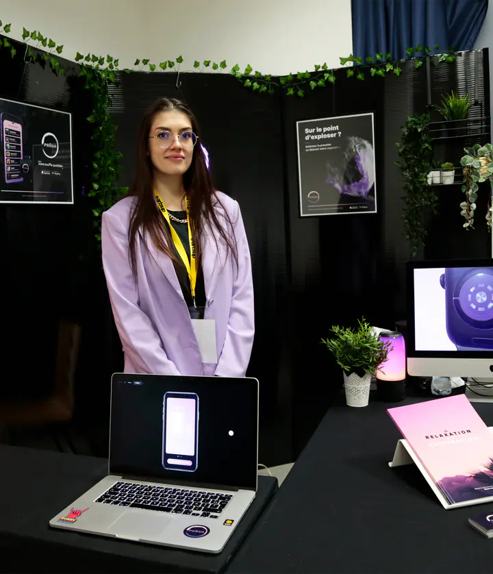 Le stand de présentation de Prana : une jeune femme en veste lilas, l’application sur un ordinateur portable, l’affiche et le livret « Relaxation »