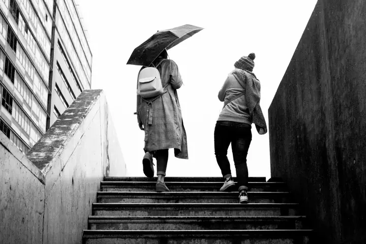 Deux personnes montent un escalier, l’une sous un parapluie