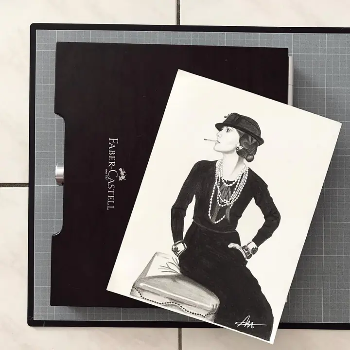 Dessin d’une femme en tailleur noir, chapeau et sautoirs de perles, posé sur une boîte de crayons