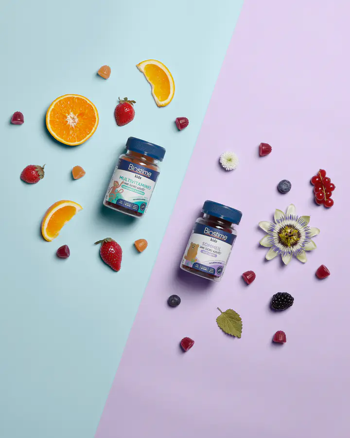Deux piluliers Biostime entourés d’oranges, de fruits rouges et d’une fleur de la passion, vus de dessus