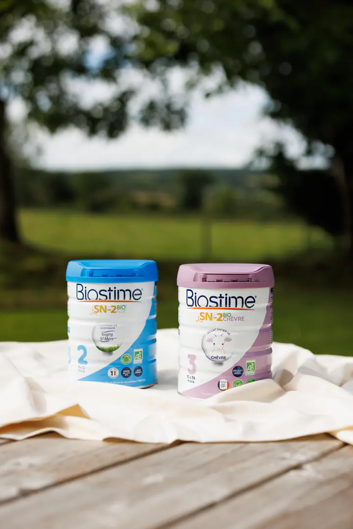 Deux boîtes de lait Biostime sur une nappe, devant un champ