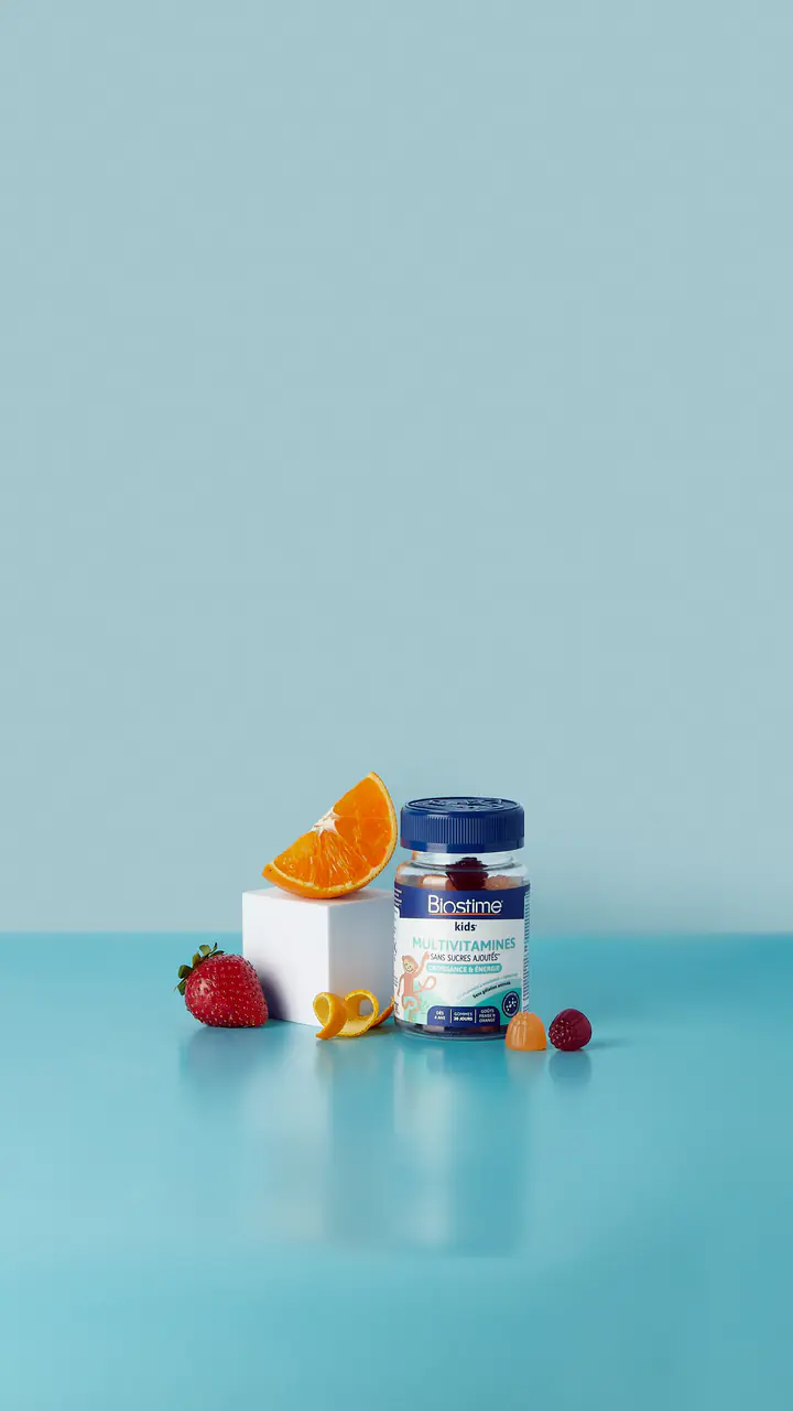 Un pilulier Biostime sur un cube blanc, avec une tranche d’orange et des fruits rouges, sur fond bleu
