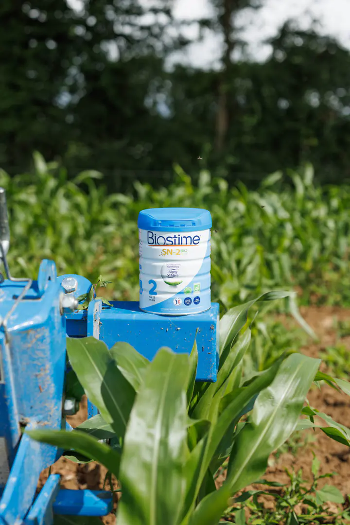 Une boîte de lait Biostime sur une machine agricole bleue, dans un champ de maïs