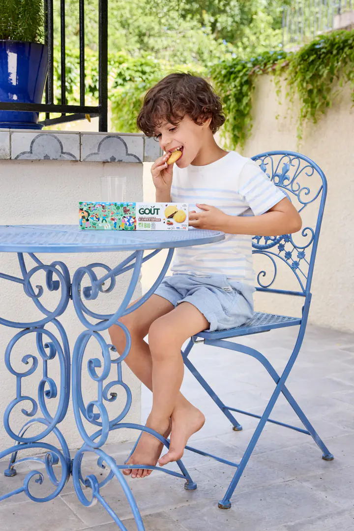 Un enfant goûte, assis à une table de jardin en fer forgé bleu