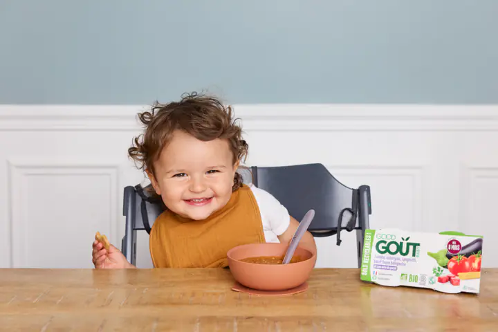 Un bébé souriant à table, devant un bol orange