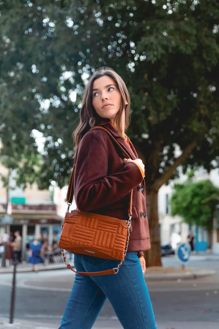Une femme en veste bordeaux, un sac matelassé camel à l’épaule, au coin d’une rue