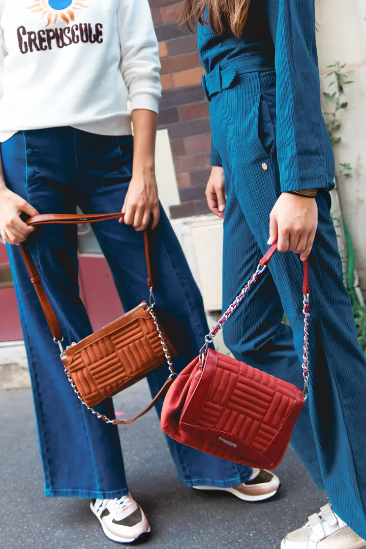 Gros plan sur deux sacs matelassés, l’un camel, l’autre rouge, portés avec des jeans