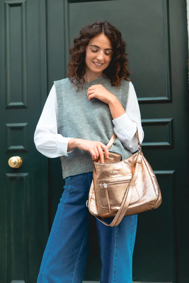 Une femme en pull sans manches gris ouvre un sac doré devant une porte verte