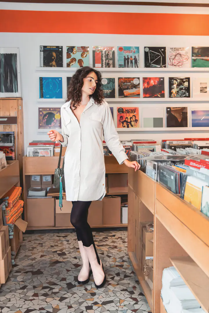 Une femme en robe chemise blanche et bottines dans les rayons d’un disquaire